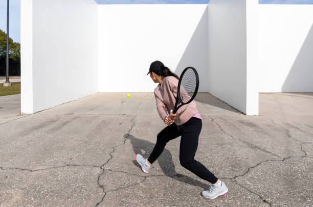 Young female athlete practicing tennis against a handball court wall stock photo