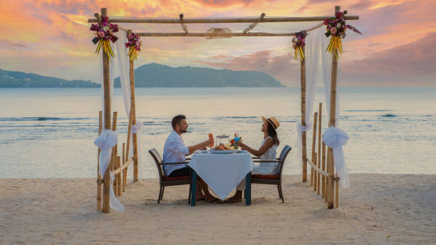 Romantic dinner on the beach in Phuket Thailand, couple man and woman having dinner on the beach Romantic dinner on the beach in Phuket Thailand, couple man and woman mid age Asian woman and European man having dinner on the beach in Thailand during sunset. phuket beach party stock pictures, royalty-free photos & images