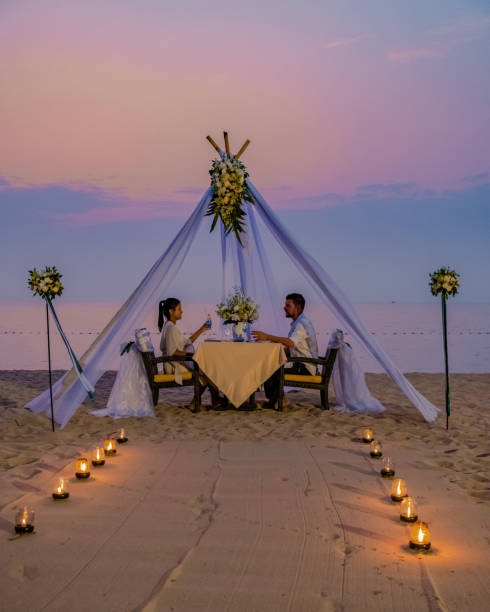 Romantic dinner on the beach in Phuket Thailand, couple man and woman having dinner on the beach Romantic dinner on the beach in Phuket Thailand, couple man and woman mid age Asian woman and European man having dinner on the beach in Thailand during sunset. phuket beach party stock pictures, royalty-free photos & images