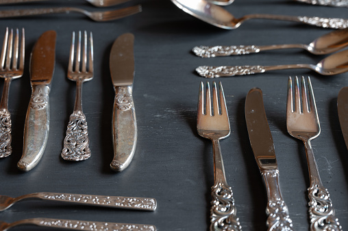 An assortment of silver knives, spoons, and forks on a dark background.