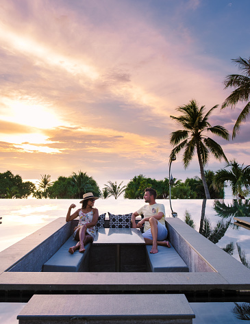 couple watching the sunset in an infinity pool on a luxury vacation in Thailand, man and woman watching the sunset on the edge of a pool in Thailand on vacation