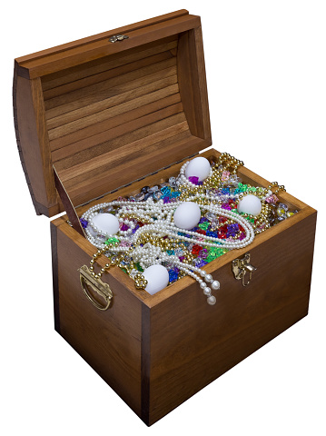 Close-up photo looking down at a wooden treasure chest over-flowing with jewels, pearls, beads and white chicken eggs isolated on a white background. Copy space