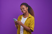 Young happy African American woman using phone stands in purple studio