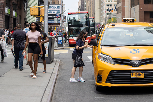 New York, NY, USA - July 5, 2022: A woman hails a yellow cab in Midtown Manhattan, New York City.