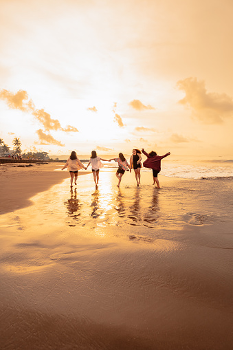a group of Asian women is running with their friends happily on the beach in the afternoon