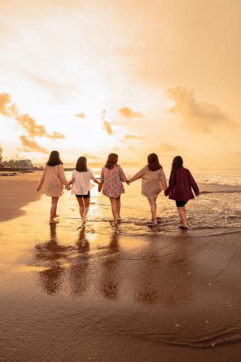 a group of Asian women is running with their friends happily on the beach in the afternoon