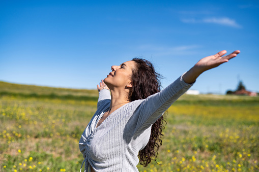 Excited Woman Raising Arms In Yellow Field With Blue Sky Background Celebrating Spring