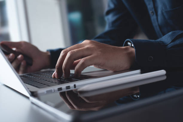 istock Man using mobile phone and working on laptop computer at home office. Casual business man freelancer online working, surfing the internet on smartphone, portable computer devices 1460167335