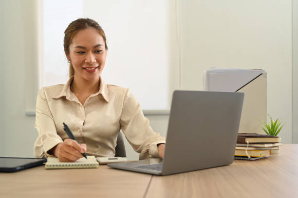 istock Pretty asian female office worker working with laptop computer and writing importance information on notepad. 1460167554