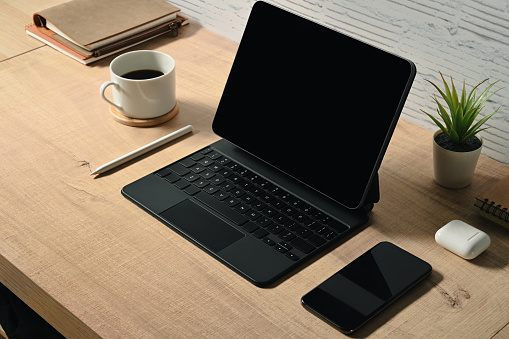 Tablet, keyboard, books, notepad, reading glasses, ear buds, and pens on workspace