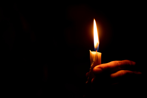 candle flame illuminates a female hand in a room