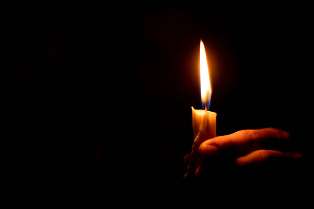 candle flame illuminates a female hand in a dark room stock photo