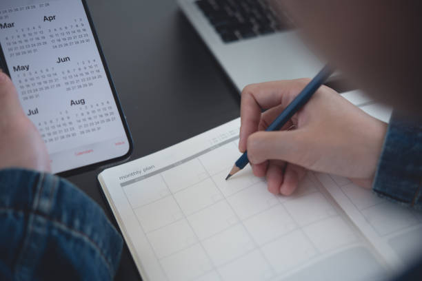 istock 2023 Calendar event planner timetable agenda plan on organize schedule. Business woman using mobile phone with monthly calendar for event planning, Plan scheduling on notebook with laptop on office table 1460169907