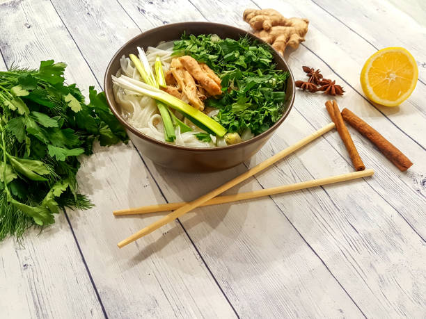 Traditional Fo Bo soup with beef, rice noodles, ginger, lemon in a bowl on a white wooden background. Vietnamese and Asian cuisine.