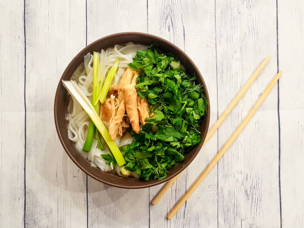 Traditional Fo Bo soup with beef, rice noodles, ginger, lemon in a bowl on a white wooden background. Vietnamese and Asian cuisine.