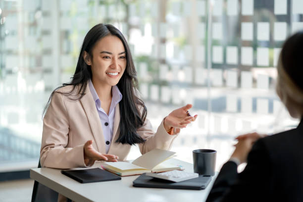 Two young Asian business woman talk, consult, discuss working with new startup project idea presentation analyze plan marketing and investment in the office. stock photo