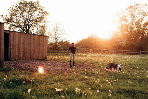 proud young female cowgirl in farm looking away with dog on sunset