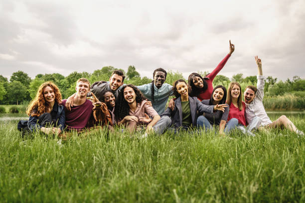 Happy friends hug each other as they meet in the park. Group of cheerful young diverse multiethnic people enjoying good summer weather, spending time in a green sunny park and having fun together