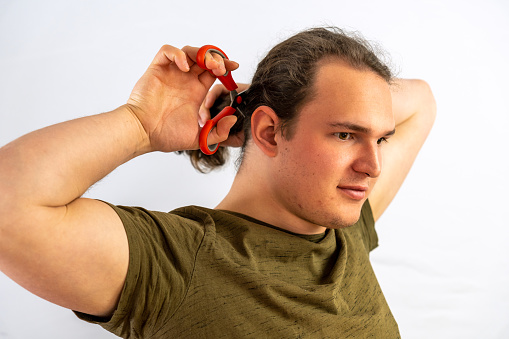 A vertical portrait of a male tying his long blonde hair