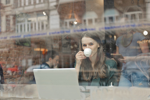 A beautiful white woman drinking coffee at the cafe with her laptop in front of her