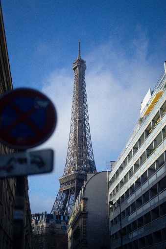 Paris, France – January 13, 2023: A vertical shot of the Eiffel tower seen from the street on blue cloudy sky background