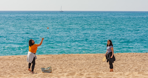 A sunny day at a beach in Spain with two young Hispanic girls playing tennis