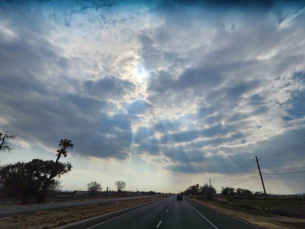 istock The sky with sun rays breaking through the clouds and a road surrounded by plants and trees 1460195100