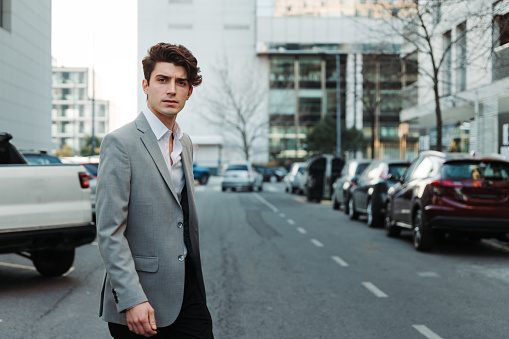 A serious young Caucasian guy dressed professionally walking on a street