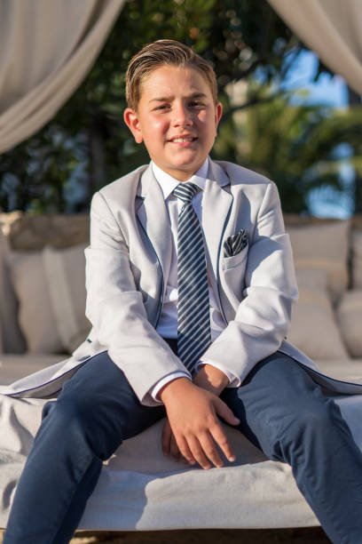 istock Vertical closeup of a young boy in a light gray blazer sitting on the sofa. 1460196584