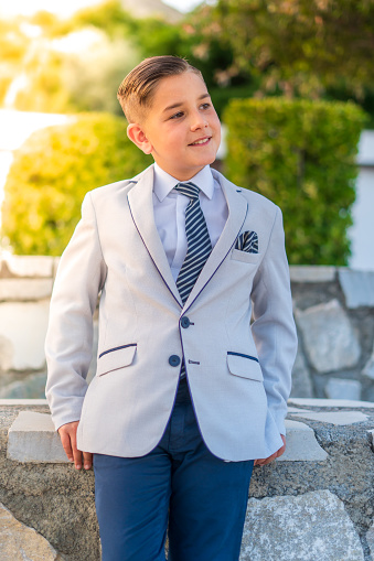 A vertical shot of an adorable male child in a formal suit outfit posing
