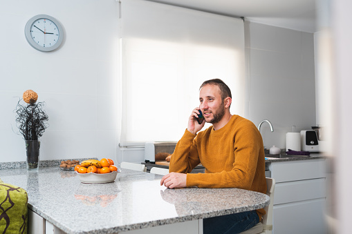 A caucasian male in an orange blouse sitting at the table with fruits and talking on the phone