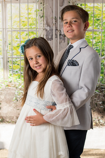 A vertical shot of a pair of male and female siblings posing in formal outfits
