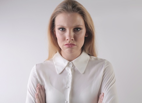 A portrait of an angry young blonde female with crossed arms on a white background
