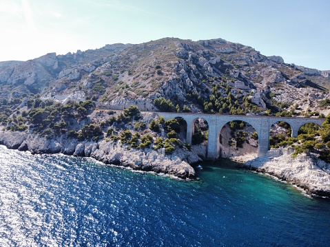 An aerial of a bridge near a beautiful sea with a tall mountain in the background in Marseille, France