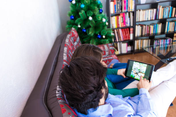 istock Young couple using their tablet sitting on a couch near the Christmas tree 1460198700