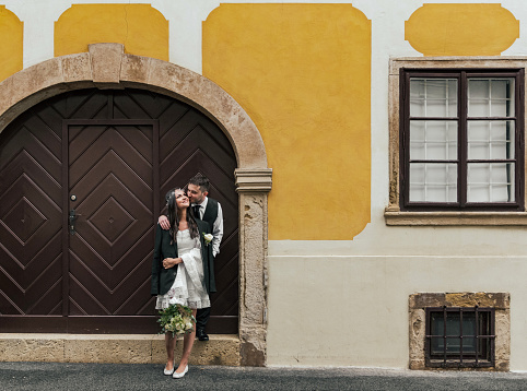 Beautiful bride and groom standing in front of wooden door on yellow building at Gornji Grad in Zagreb, Croatia.