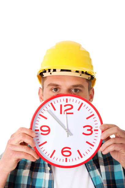 istock Young engineer in a helmet holding a big wall clock 1460202345