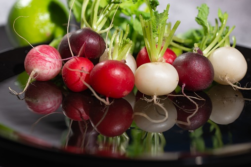 A closeup of colorful radishes reflecting in a metallic plate