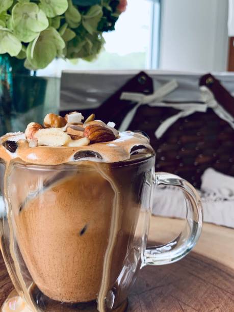 Vertical shot of a foamy coffee with nuts on it and a bouquet in the blurred background