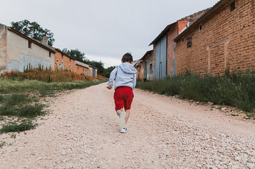 The little boy in red shorts and a gray hoodie running outdoors.