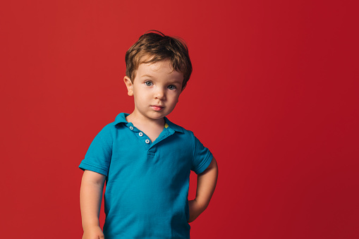 A closeup of a young boy in a blue t-shirt on a red background.