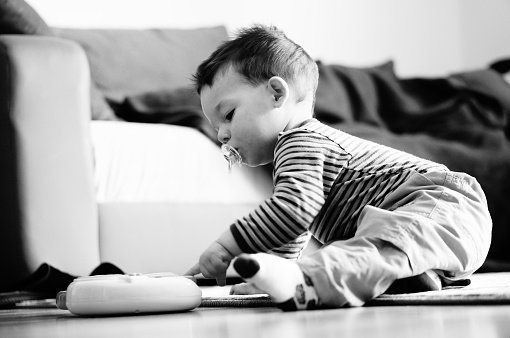 A Caucasian little boy sitting on a carpet and playing with a plastic toy