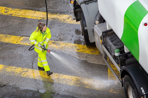 Santiago de Compostela, Spain – January 17, 2023: Woman worker cleaning a city road with high pressure water of a maintenance truck. Public maintenance concept