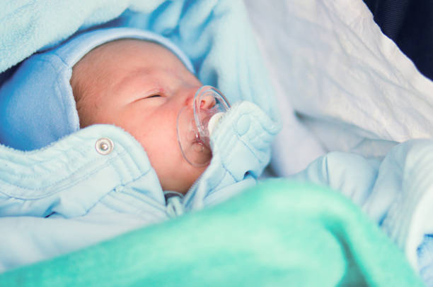A close up of a Sleeping baby with a pacifier in a blue blanket