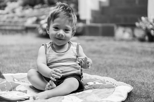 A grayscale shot of a cheerful Polish toddler sitting on the play nest in the park