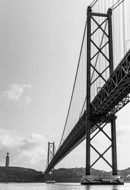 istock Vertical low angle grayscale of 25 de Abril Bridge under the sky and clouds 1460208807