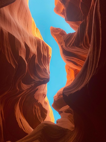 A vertical low-angle shot of blue sky seen through orange walls of the Navajo Upper Antelope Canyon