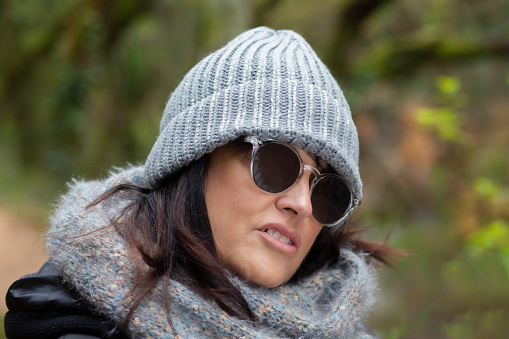 A woman with sunglasses and wool hat walks in the forest on an autumn day in the morning. close up portrait in the forest in autumn.