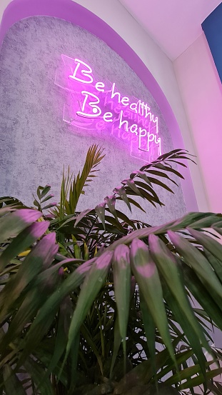 A pink neon sign saying be healthy be happy in a cafe