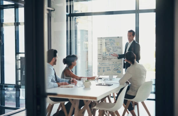 istock Business people, presentation management meeting in workspace on whiteboard, workshop or target idea. Mentor, manager and seminar planning in workplace with notes, teamwork agenda or company training 1460217527